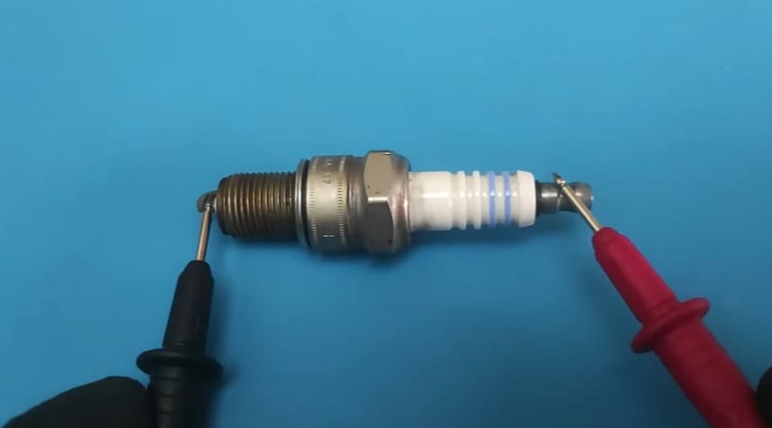 A person testing a spark plug with a multimeter