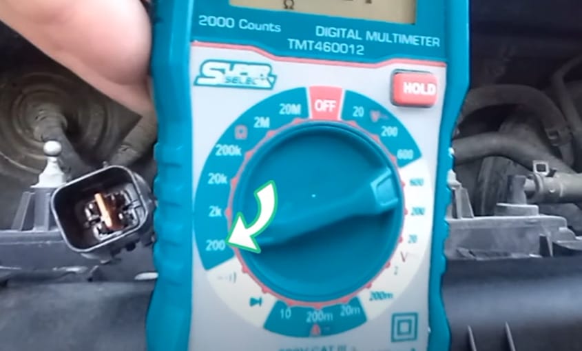 A person is using a multimeter to test the oxygen sensor of a car