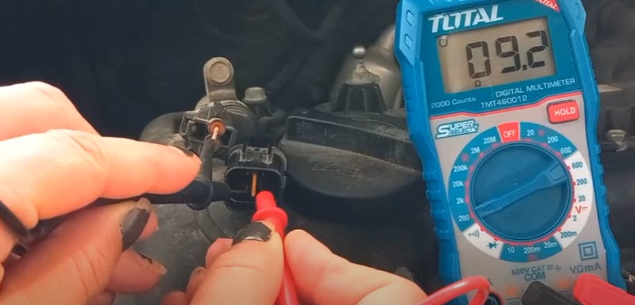 A person is using a multimeter to test a car's O2 sensor