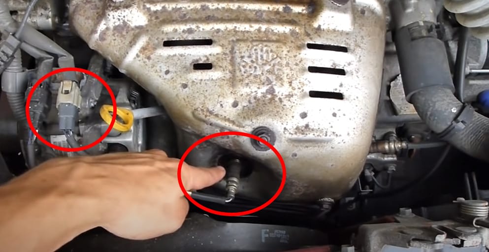 A person is pointing at the 02 sensor of a car