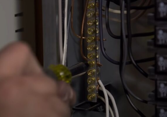A person is working on an electrical panel using a screwdriver