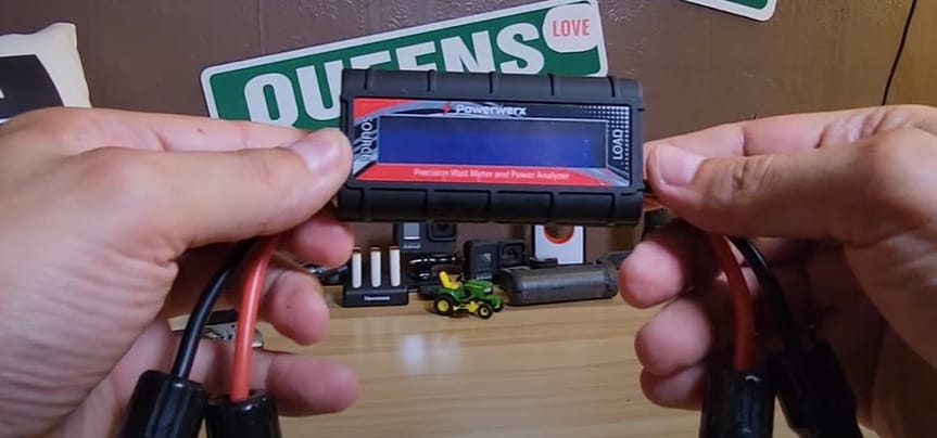 A person is conducting solar panel testing, holding a battery meter in front of a table