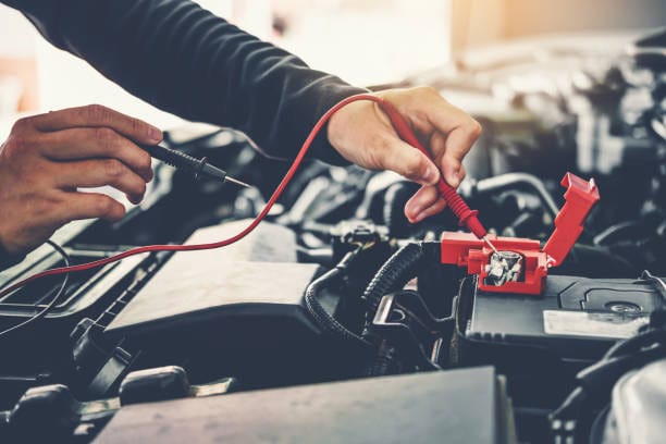 A man is using a multimeter to work on a car battery