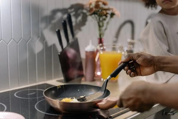 A man is frying eggs in a frying pan on a stove