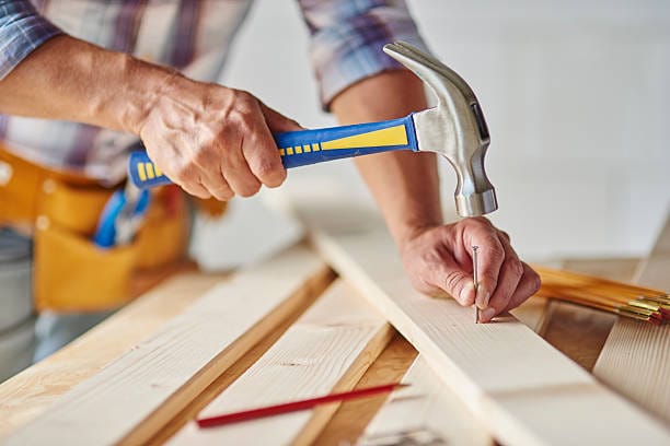 A man is hammering a piece of wood with a nail