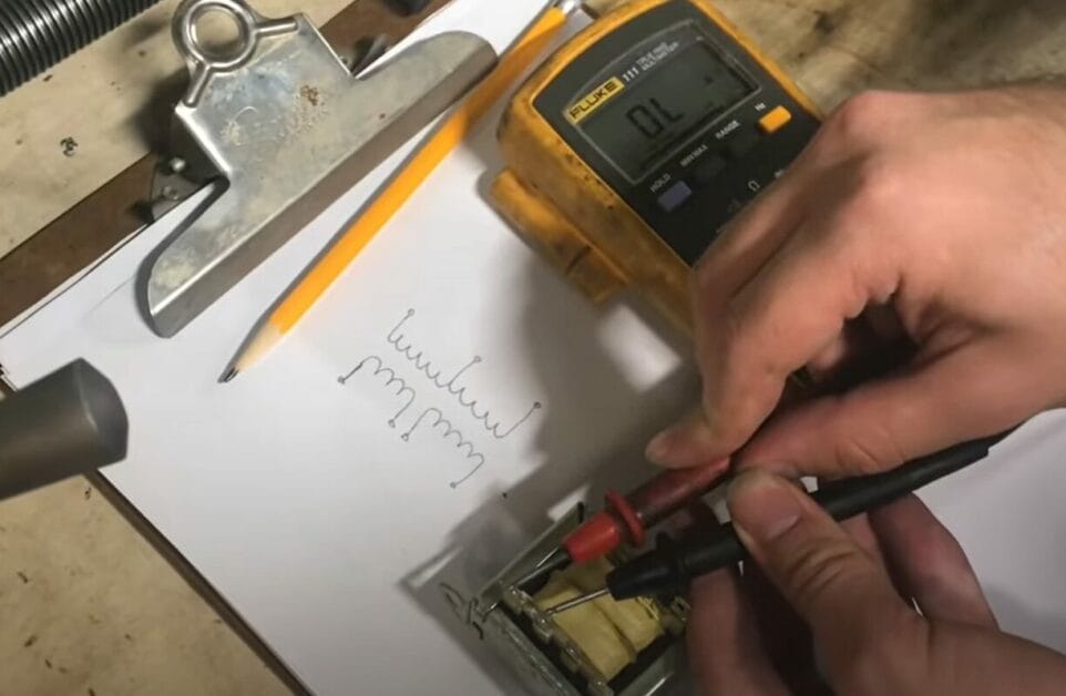 A person testing a transformer with a multimeter on a piece of paper