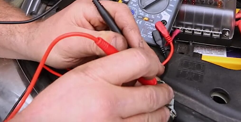 A person is using a multimeter to measure the resistance of a car battery