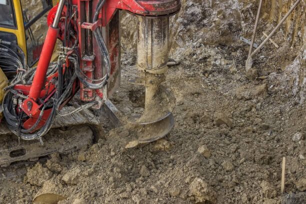A red excavator digging in the dirt to drill a well