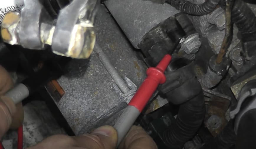A person is working on a car battery and testing the starter using a multimeter