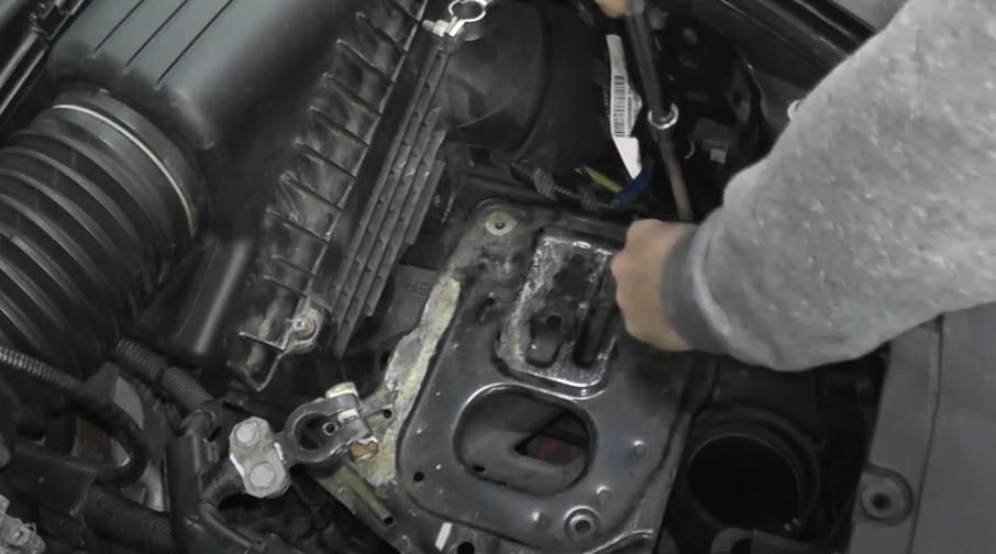 A man is working on the engine of a car, testing the starter