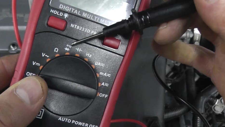 A person using a multimeter to test a starter on a car engine