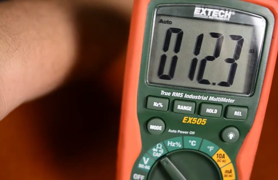 A person holding a multimeter with 012.3 reading in it