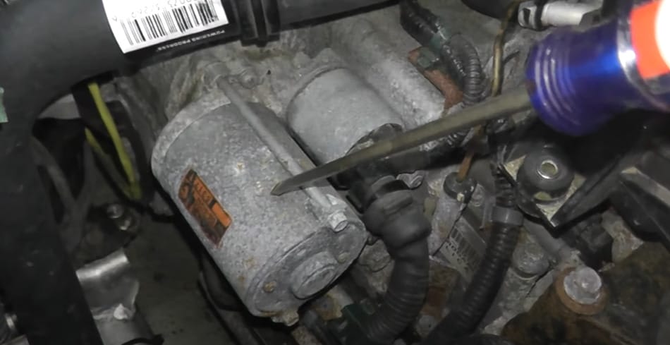 A man is working on the engine of a car, testing the starter