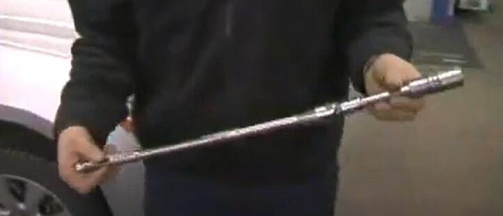 A man demonstrating how to use a breaker bar in front of a car