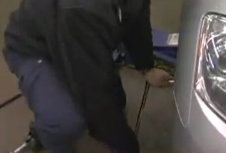 A man is using a breaker bar while working on a car in a garage