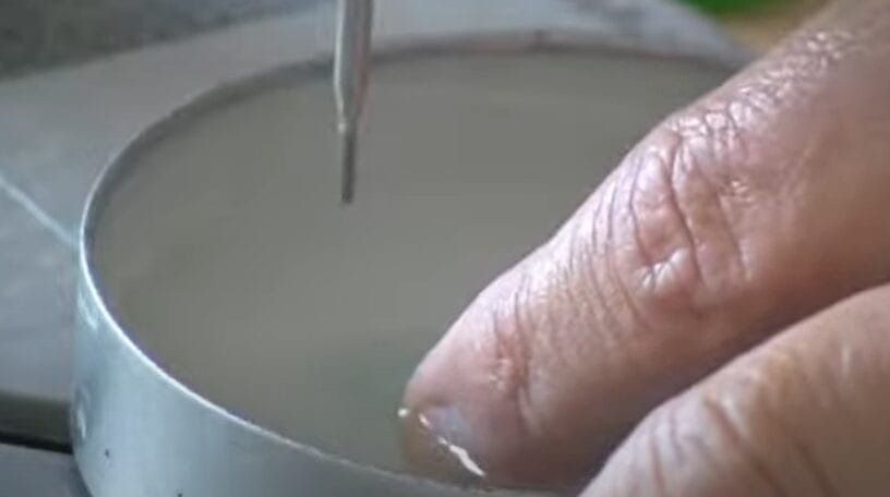 A person pouring liquid into a cup while demonstrating how to drill a hole in sea glass