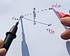 A person is drawing a diagram on a piece of paper to illustrate the process of testing a 5 pin relay with a multimeter