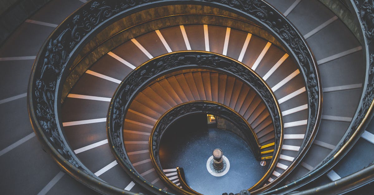Aerial view of a spiral staircase with ornate railings, showcasing a circular design and illuminated steps that create a symmetrical and visually striking pattern.