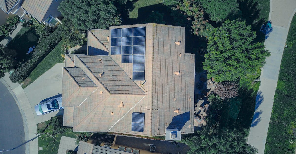 Aerial view of a house with solar panels installed on its roof, surrounded by trees, with a car parked in the driveway.