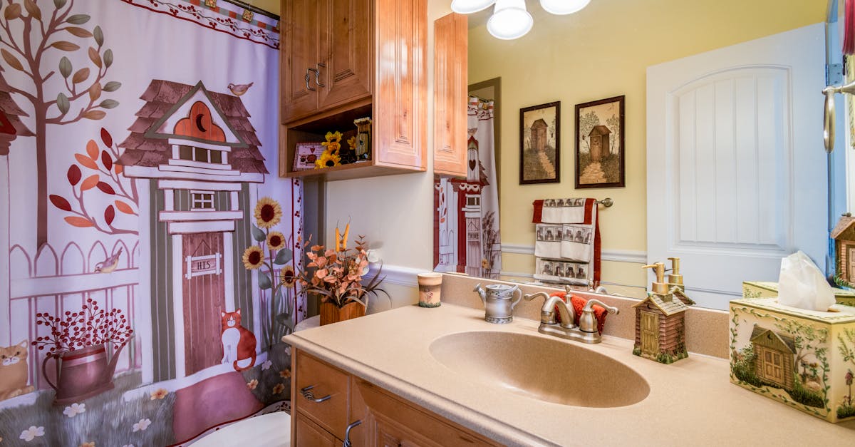 Bathroom with a beige countertop, wooden cabinets, decorative items, and a shower curtain featuring whimsical house and animal illustrations.