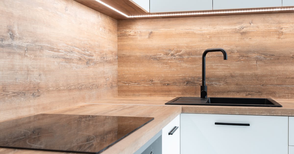Modern kitchen with a wooden backsplash and countertop, black sink and faucet, white cabinets, and a built-in electric cooktop.