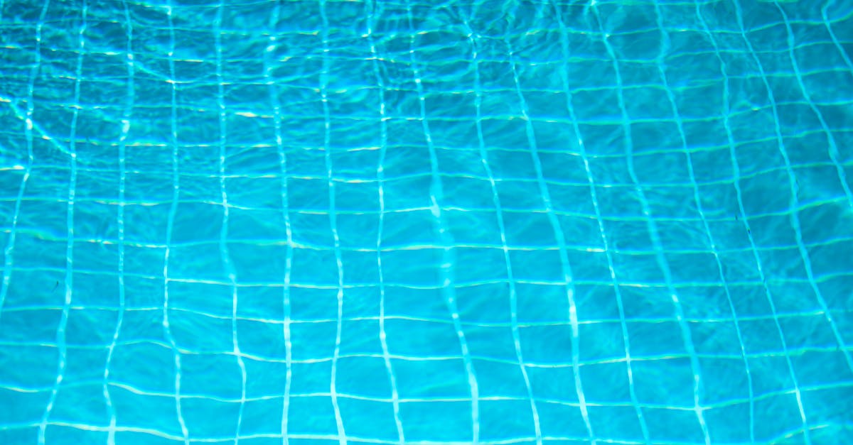 Close-up view of a tiled swimming pool floor with sunlight reflecting on the water's surface, creating rippling light patterns.