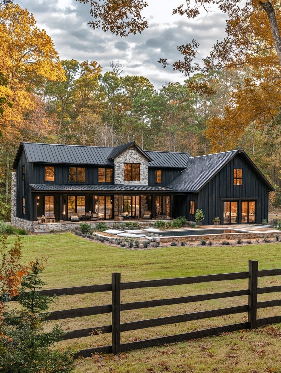 Modern two-story black house with large windows, stone accent, metal roof, and spacious patio, set in a wooded area with a grassy lawn and wooden fence in the foreground.