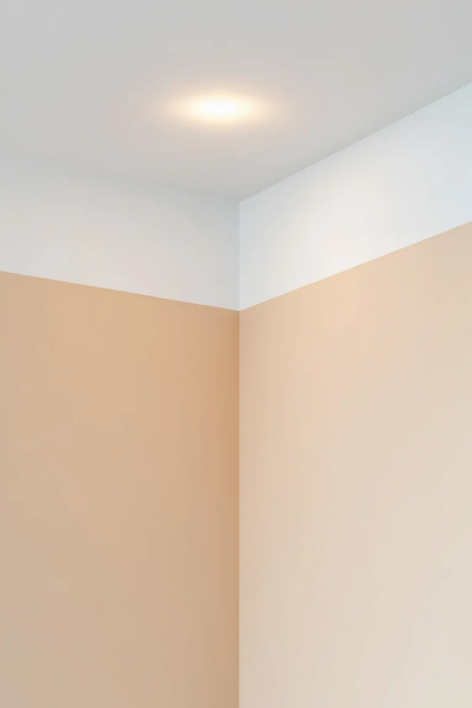 A brightly lit corner of a room with beige walls and a white ceiling, featuring a recessed ceiling light.
