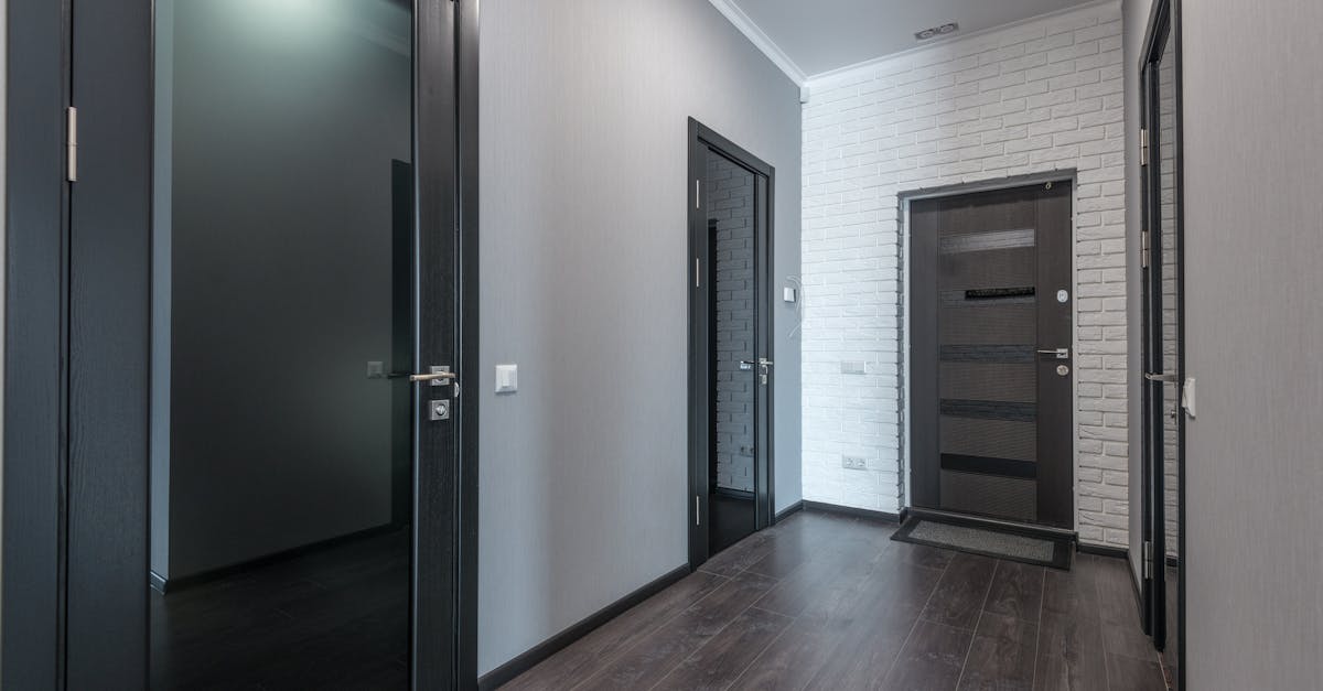 A modern hallway with dark wooden floors, light gray walls, black doors, and a white brick accent wall near the entrance door.