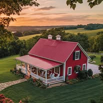 A red farmhouse with a white porch sits on a green lawn, surrounded by fields and trees at sunset.