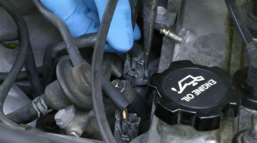 mechanic in blue gloves unplugging the fuel injector connectors