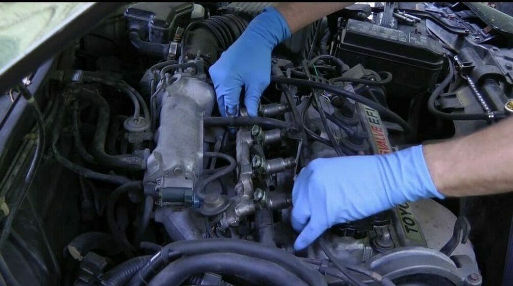 mechanic with blue gloves lifting off the fuel rail