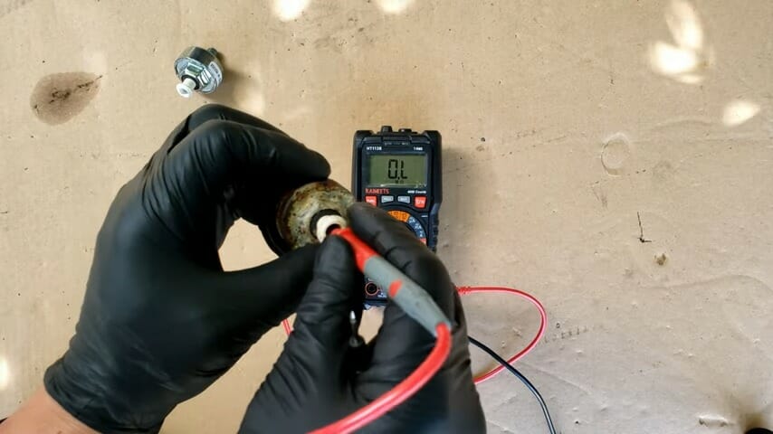 mechanic in black gloves testing knock sensor using multimeter