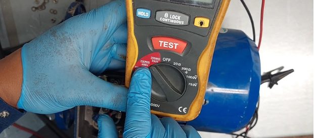 mechanic in blue-green gloves testing single phase motor with multimeter