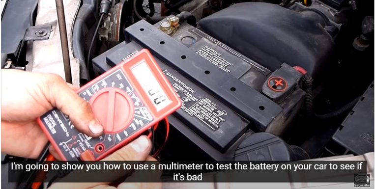 mechanic testing car's battery with a multimeter