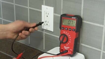 man putting black probe of multimeter to the wall outlet