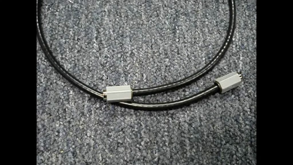 Black coaxial cable with white tip in a gray carpeted floor