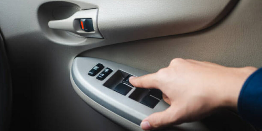 driver hand pressing car window controls button