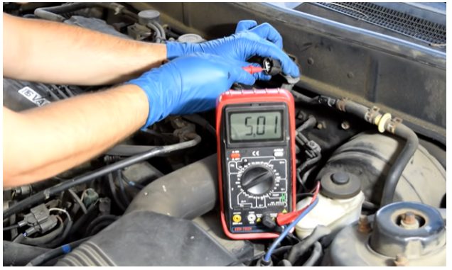 mechanic with blue gloves testing sensor with multimeter reading at 5.01