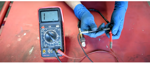 man in blue gloves testing the air fuel sensor with multimeter at a reading of 1v