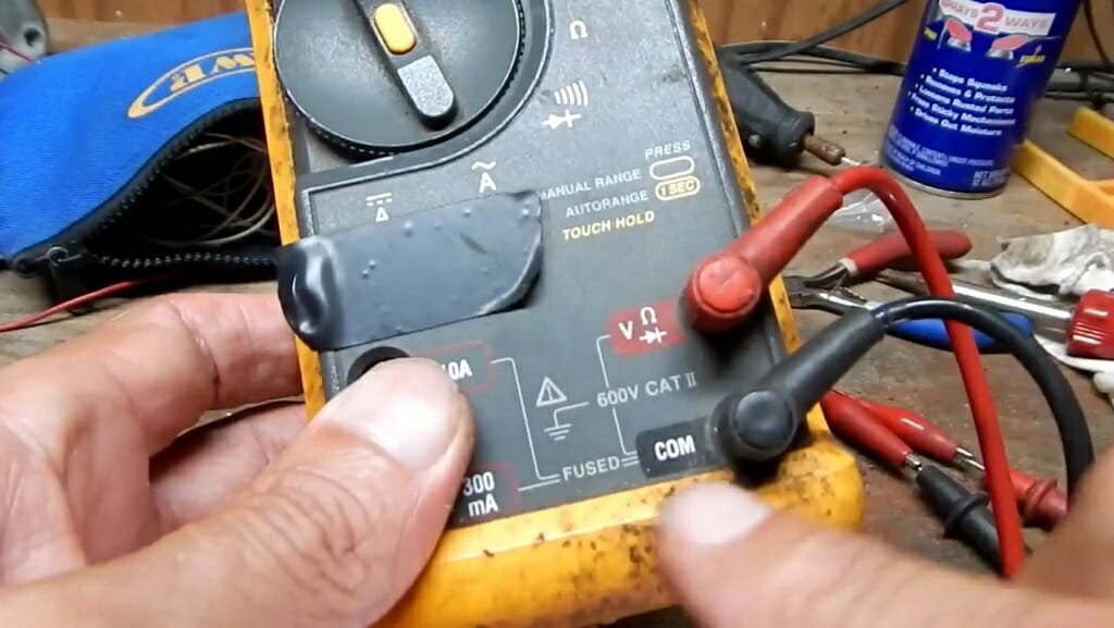 technician holding a multimeter with red and black probes plugged