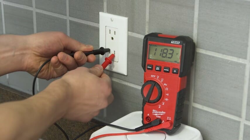 technician putting the black and red multimeter's probe to the wall outlet with reading 118.3v