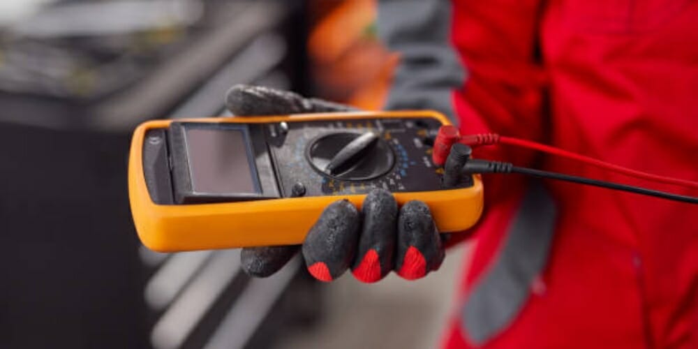 technician in glove and red suit holding a yellow multimeter
