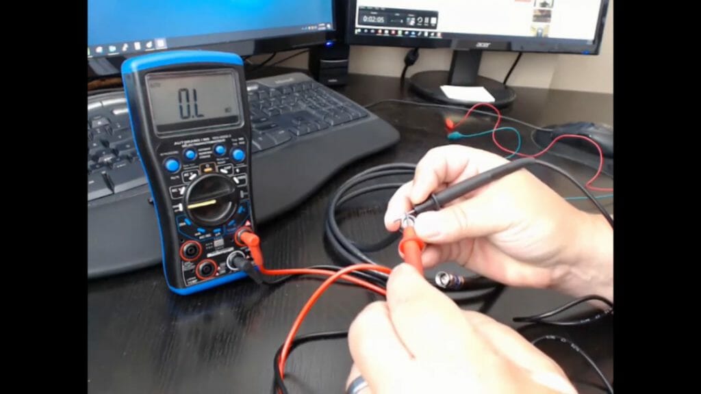technician holding multimeter probe and testing coaxial cable
