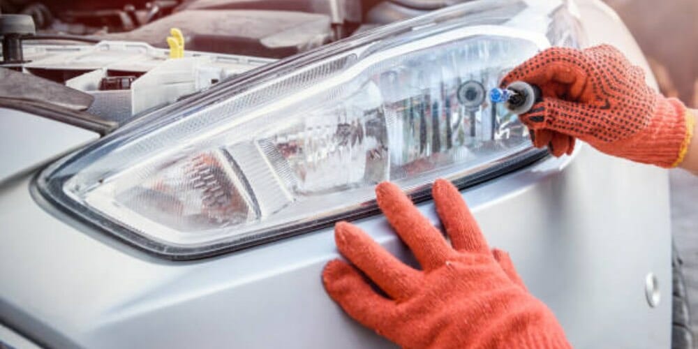 mechanic in an orange gloves holding a headlight bulb