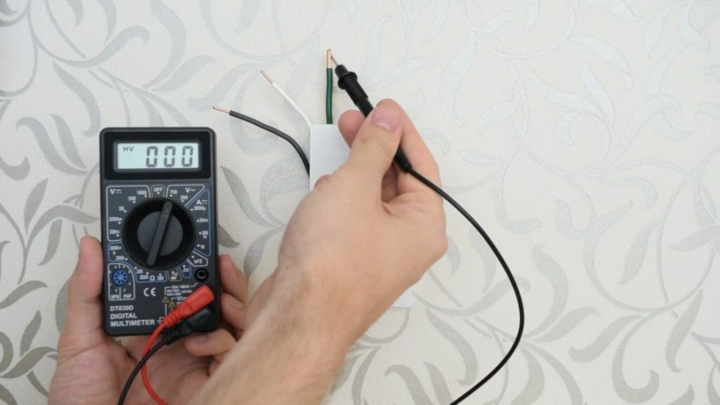 man holding multimeter at 0 reading with black probe point to a green wire