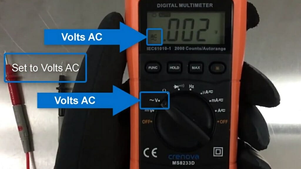mechanic with black gloves holding a multimeter at a .002v reading