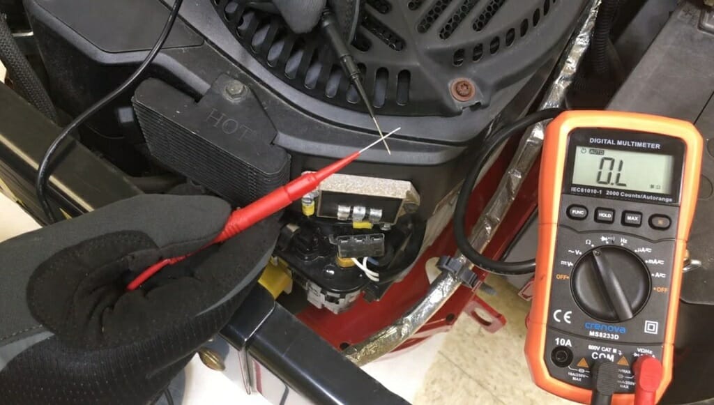 mechanic with black gloves holding red and black multimeter probe at an intial 0L reading