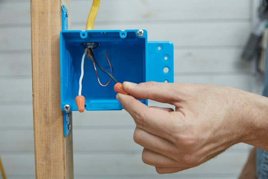 a hand pushing the capped wire into the blue electrical box
