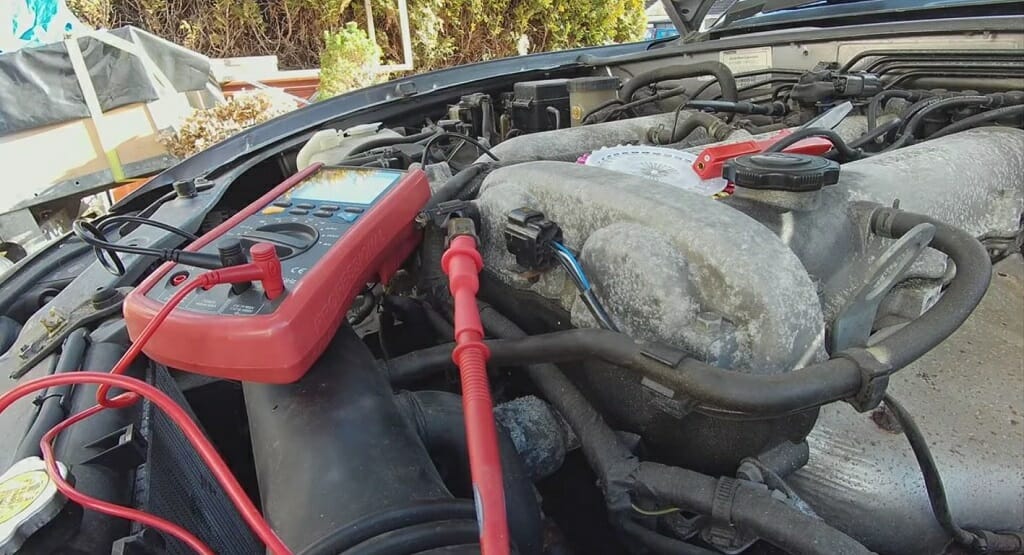 A multimeter at the top of an open hood car with the oxygen sensor